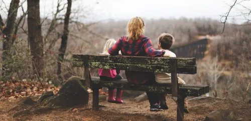 Three people sit on a bench overlooking a forested landscape.