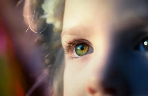 Close-up of a child's green eye with soft sunlight and shadows.
