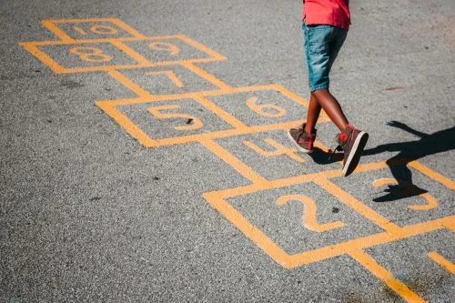 Child playing hopscotch on a numbered grid painted on asphalt.
