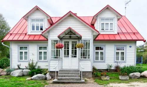 White house with red roof, attic windows, front porch, and hanging flower baskets.