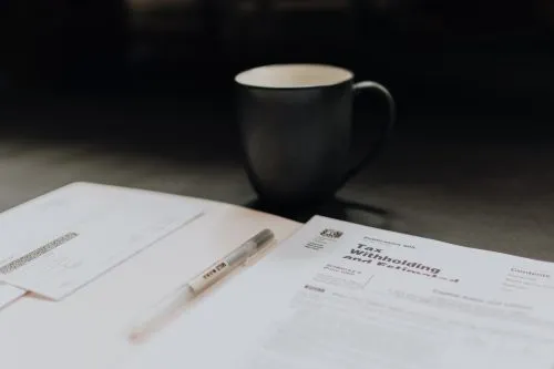 Tax forms and a pen on a table with a coffee mug in the background.