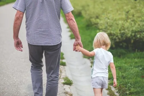 An adult and child walk hand in hand along a path bordered by grass.