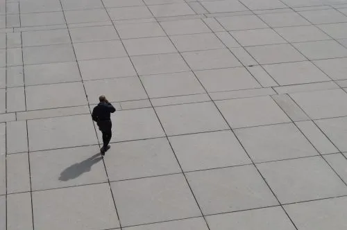 Person walking alone on a large, tiled surface.