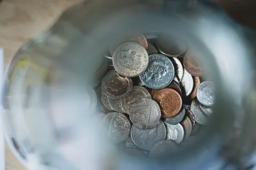 View of coins inside a glass jar from above.