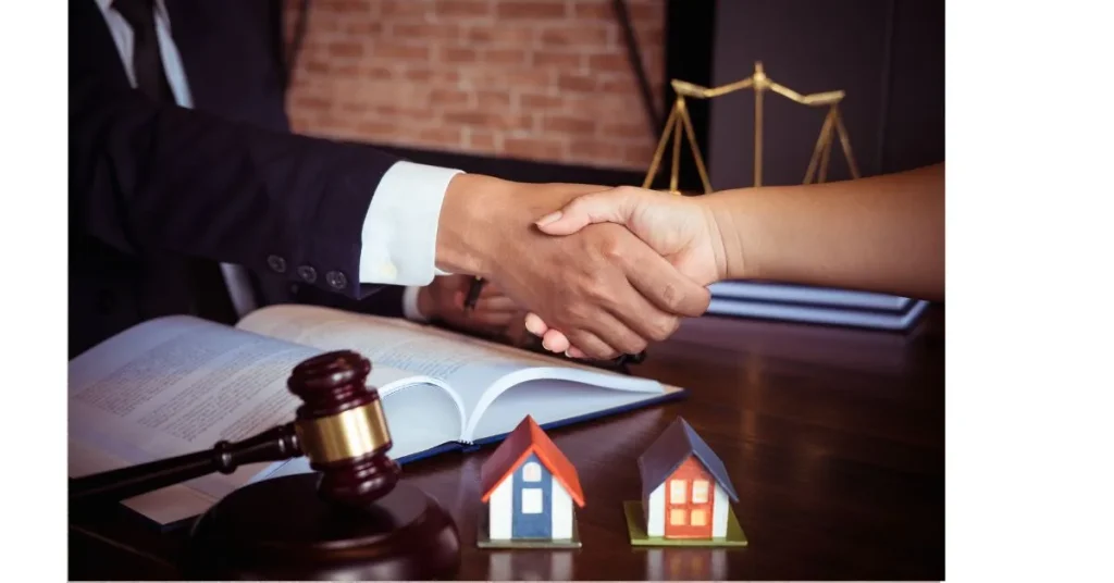 Two people shaking hands over a legal document with a gavel and model houses in the foreground.