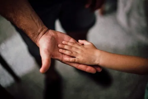 A child's hand rests on an adult's open palm, symbolizing connection and support.
