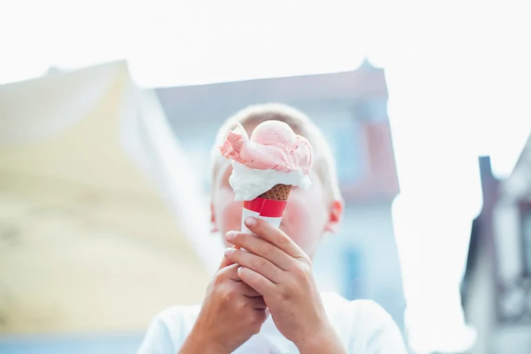 Child holding a large pink and white ice cream cone.