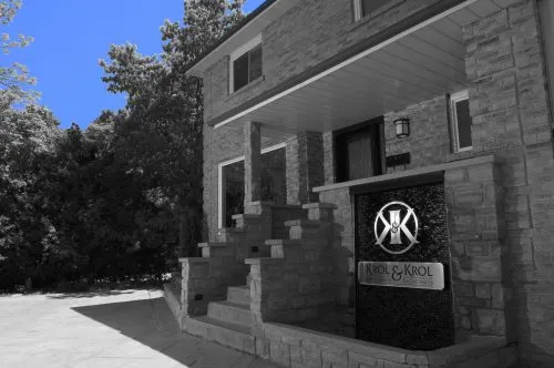 Stone building with stair entrance and a sign reading "Krol & Krol" against a black and white background, with a blue sky.