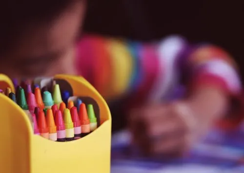 A child drawing with crayons beside a yellow crayon box.