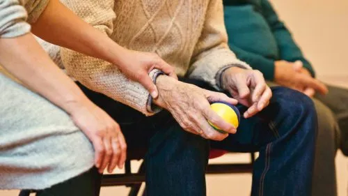A person assists an elderly individual holding a stress ball.