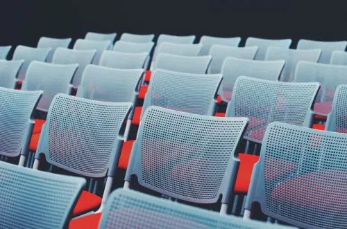 Rows of modern, white mesh chairs with red cushions in a dimly lit setting.