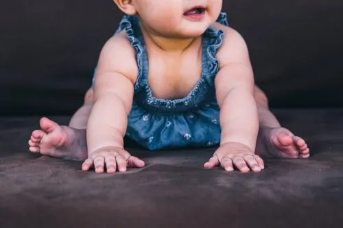 Baby in a blue outfit crawling on a dark surface.