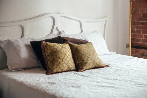 Bed with white headboard, white and dark pillows, and patterned gold cushions.