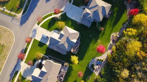 Aerial view of suburban houses with green lawns and colorful trees.