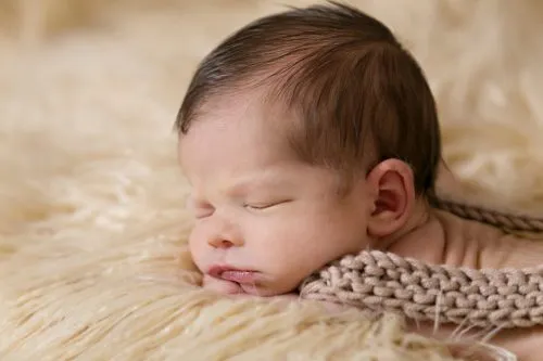 Newborn baby sleeping on a soft, fluffy surface.