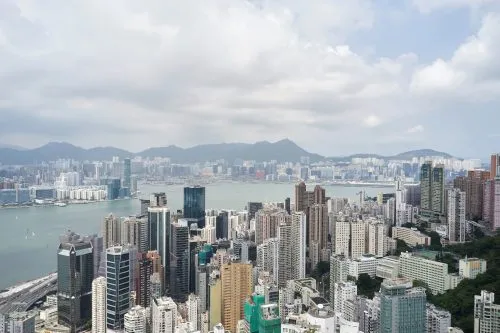 Aerial view of a dense cityscape with skyscrapers and a bay under a partly cloudy sky.