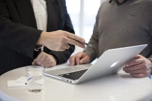 Two people discussing over a laptop, one pointing with a pen.