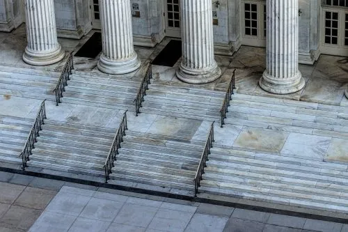 Stone steps with metal railings leading to a building with large columns.
