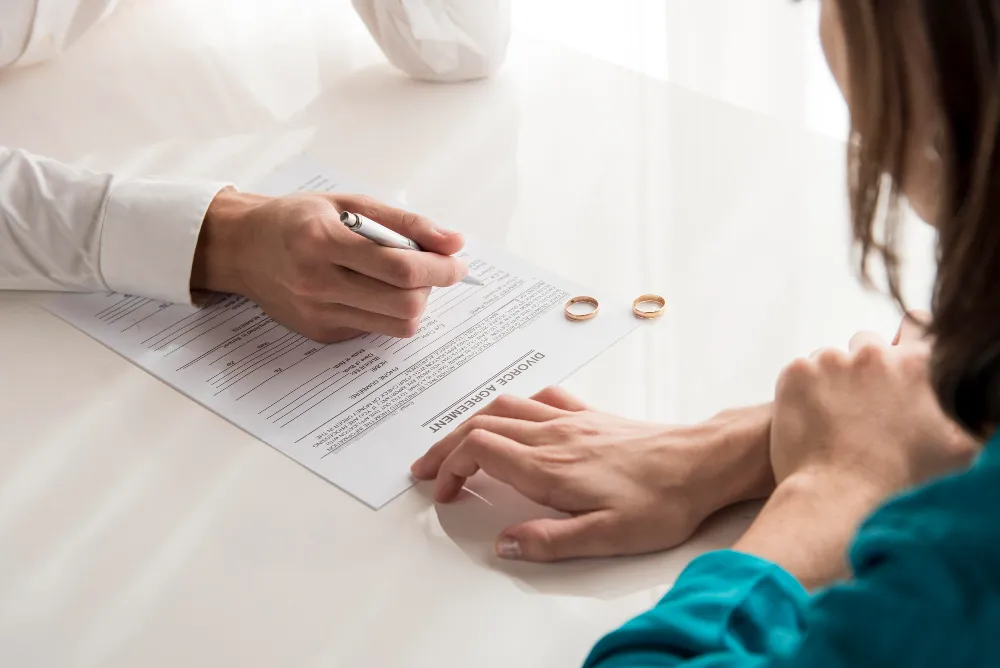 Man signing a divorce agreement with rings on the table.