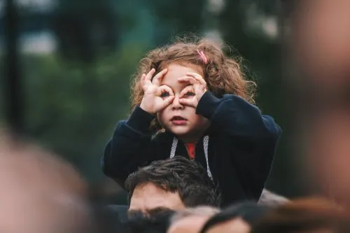 Child on shoulders making pretend binoculars with hands.