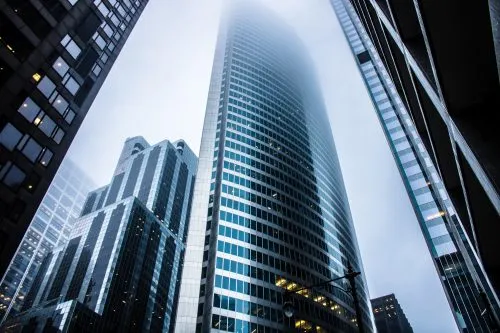 Foggy skyline with tall, modern skyscrapers viewed from street level.