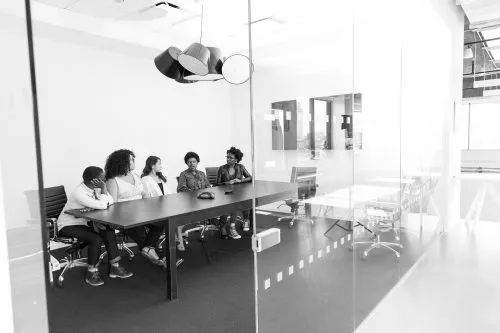 Five people sitting around a conference table in a glass-walled meeting room.