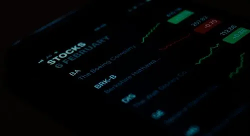 Smartphone screen displaying stock prices and graphs in a dark setting.