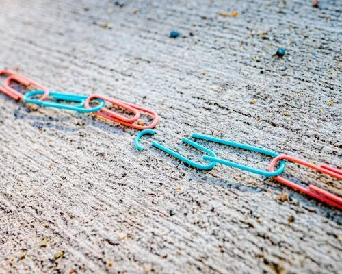 A chain of red and blue paper clips linked together on a textured surface.