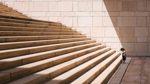 A small child stands at the base of a large stone staircase in sunlight.