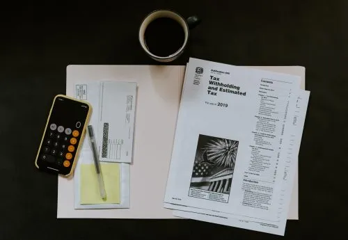 Tax documents, calculator, pen, and coffee cup on a table.