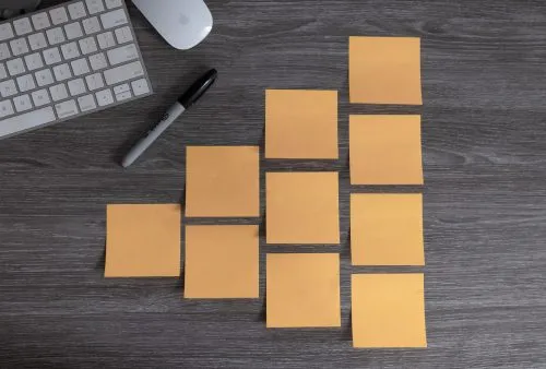 Nine orange sticky notes arranged on a gray desk next to a Sharpie and a keyboard.