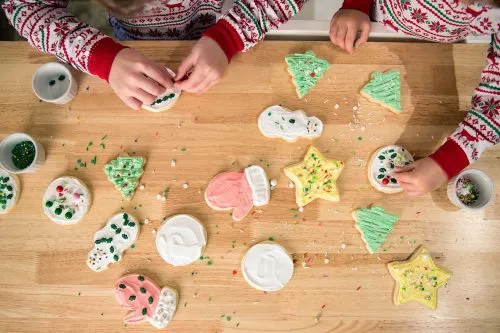 Children decorating festive cookies on a wooden table.