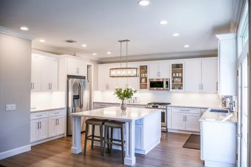 Modern kitchen with white cabinets, island, stainless steel appliances, and wood flooring.