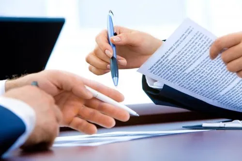 Hands holding pens and reviewing a printed document on a desk.