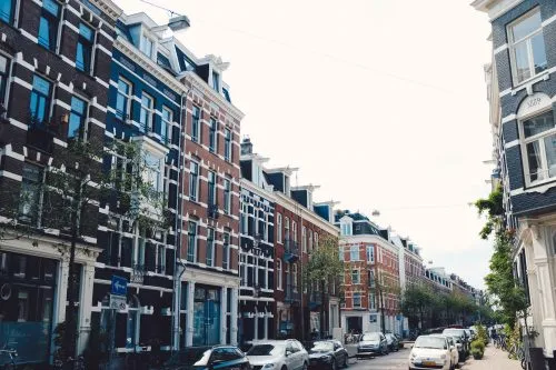 Street view with rows of colorful, traditional European buildings and parked cars.