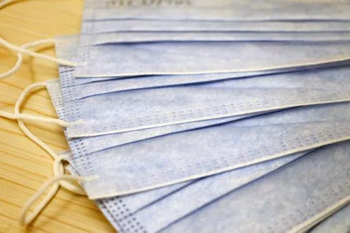 Close-up of several blue surgical masks stacked on a wooden surface.