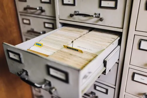 Open file drawer filled with organized index cards in an office setting.