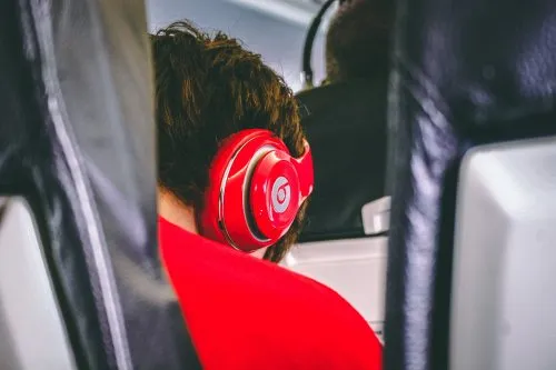 Person wearing red headphones seated on an airplane.