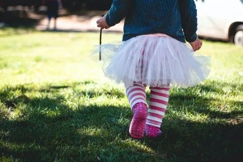 Child in a tutu and striped leggings walking on grass.