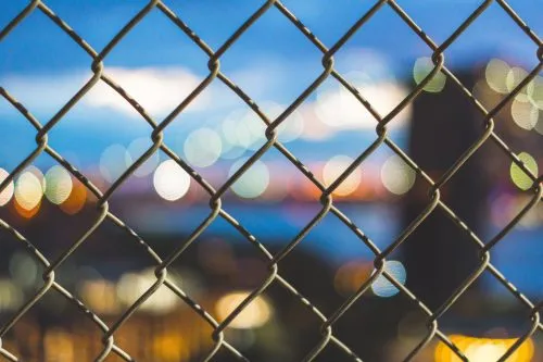 Chain-link fence with blurry city lights in the background.