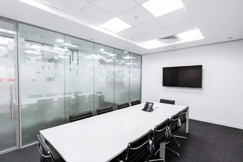 Modern conference room with a long table, black chairs, glass wall, and wall-mounted TV.