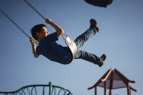 Child swinging high in the air on a playground swing set.