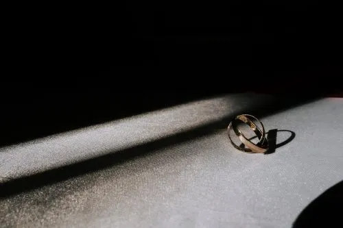 A gold ring lies in a beam of light on a textured surface.