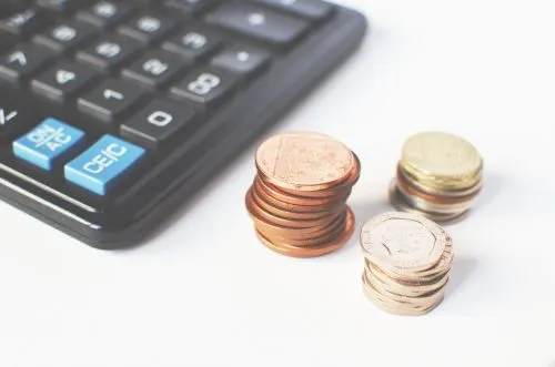 Stacks of coins next to a calculator on a white surface.