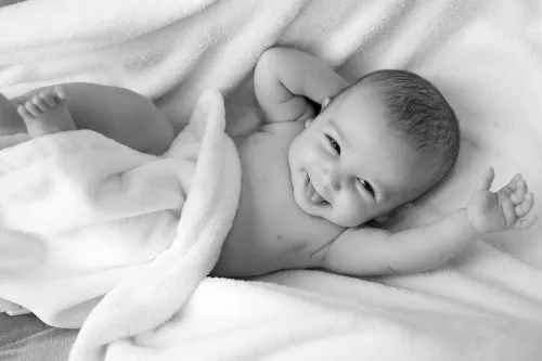 Smiling baby wrapped in a soft white blanket, lying on a bed.