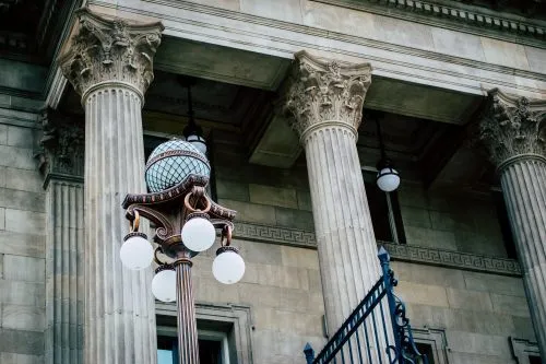 Ornate street lamp in front of a neoclassical building with columns.
