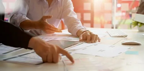 People discussing plans with documents and a tablet on a desk.
