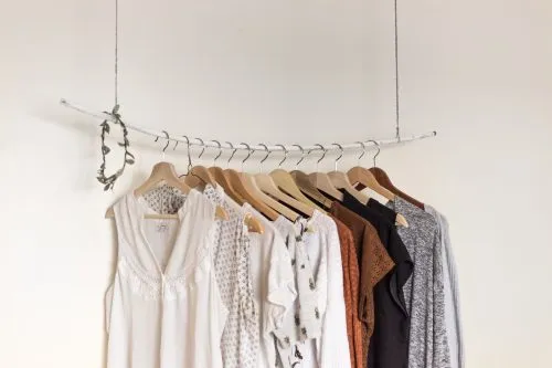 Clothes hang on a minimalist branch rack against a white wall.