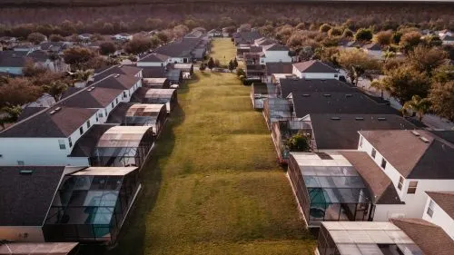Aerial view of suburban houses with enclosed patios lining a wide grassy pathway.