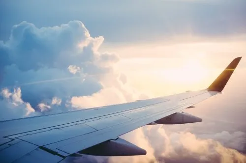 View of an airplane wing flying above clouds with a sunset in the background.